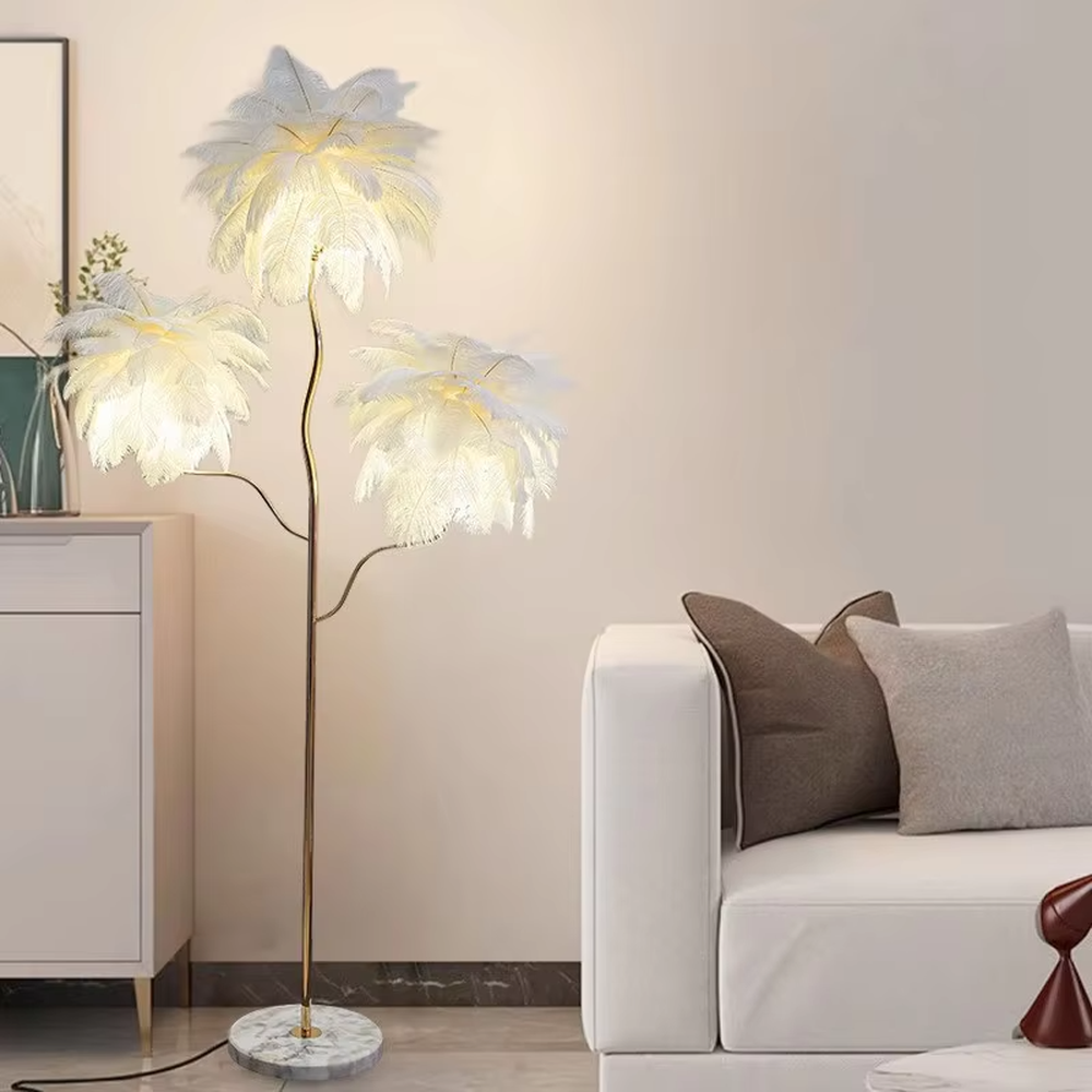 This is a light luxury soft feather-shaped floor lamp, equipped with three white feather lampshades, paired with a golden curved lamp pole and a marble base. The design is gentle and elegant, with soft and hazy lighting through the feathers. It is used for space lighting and decoration, creating a warm and soft light luxury atmosphere. Suitable for light luxury-style living rooms, bedrooms, internet-famous homestays and other places.