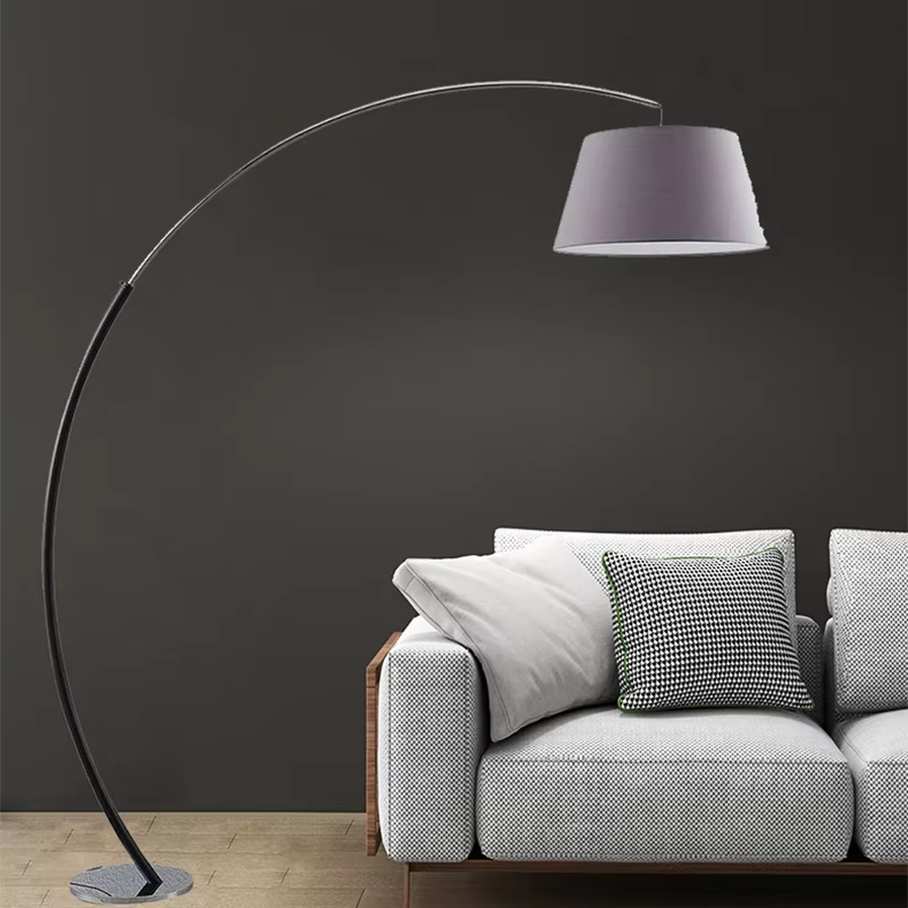 This is a modern minimalist curved floor lamp, with a black curved lamp pole paired with a light purple fabric lampshade and a silver textured disc base. The lighting is soft and warm, creating a minimalist comfortable atmosphere.