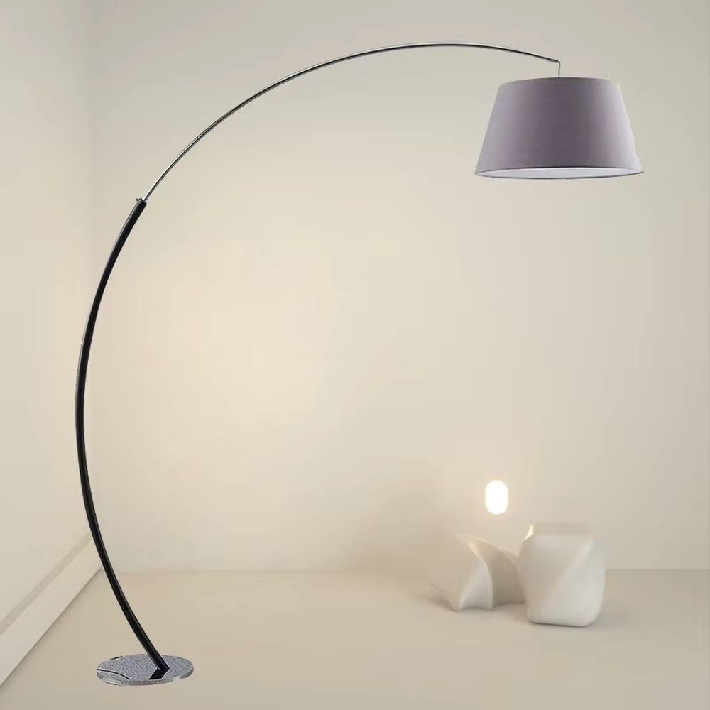 This is a modern minimalist curved floor lamp, with a black curved lamp pole paired with a light purple fabric lampshade and a silver textured disc base. The lighting is soft and warm, creating a minimalist comfortable atmosphere.