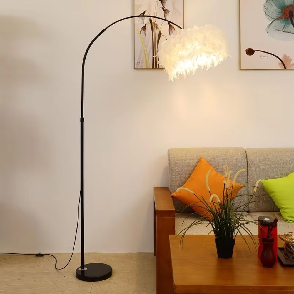 This is a warm romantic-style curved feather floor lamp, with a black curved lamp pole paired with a white feather lampshade and a black disc base. The lighting is soft and warm, creating a comfortable romantic space atmosphere.