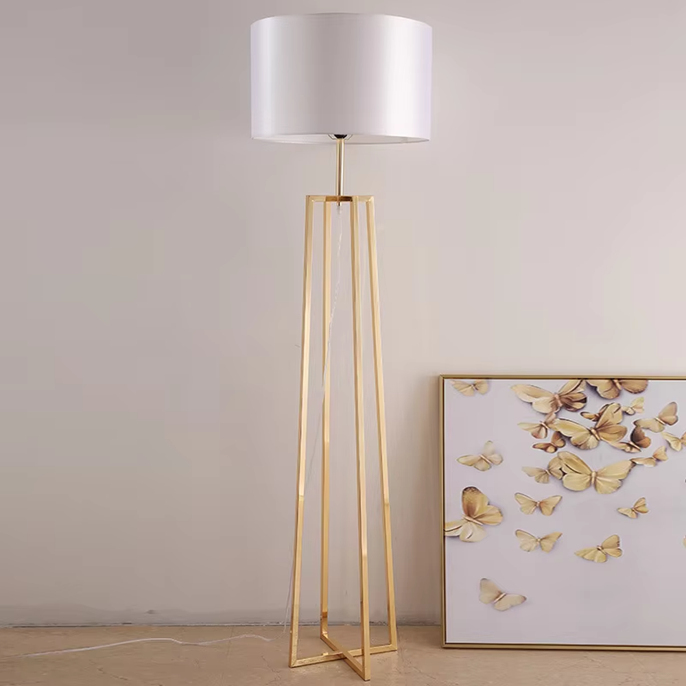 This is a light luxury minimalist golden geometric frame floor lamp, featuring a golden triangular geometric frame lamp pole paired with a white cylindrical fabric lampshade. It has a minimalist and grand design, with soft and uniform lighting. It is used for space lighting and decoration, creating a light luxury minimalist atmosphere. Suitable for light luxury-style living rooms, modern minimalist bedrooms, high-end apartments and other places.