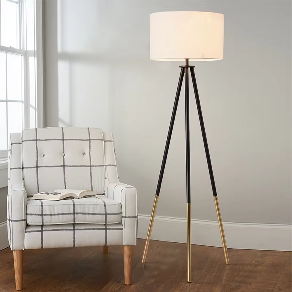Light luxury black-gold spliced tripod floor lamp, brown fabric cylindrical lampshade + black pole gold foot stand, soft lighting, creating a high-end minimalist atmosphere.