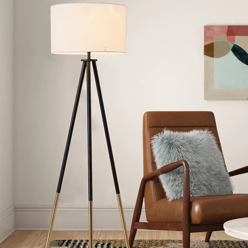 Light luxury black-gold spliced tripod floor lamp, brown fabric cylindrical lampshade + black pole gold foot stand, soft lighting, creating a high-end minimalist atmosphere.