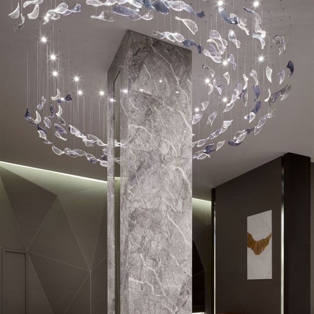 This modern artistic bird-shaped chandelier consists of transparent and gradient blue-purple leaf-shaped glass ornaments hung staggered, arranged in an arc streamline, with point light sources to create a dynamic visual effect, serving both lighting and decorative purposes, suitable for high-end commercial spaces such as luxury sales offices and hotel lobbies.
