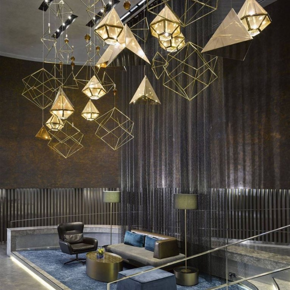 This modern geometric art chandelier is composed of intertwined gold metal lines forming an abstract frame, paired with geometric-shaped liuli/acrylic ornaments. Light refracts through them to emit a brilliant halo, serving both lighting and installation art purposes, suitable for high-ceiling commercial spaces such as hotel lobbies and high-end clubs.