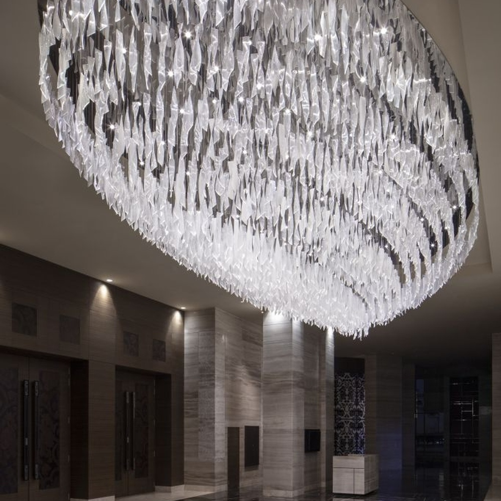 This large oval artistic chandelier is composed of a large number of transparent glass/acrylic pieces hung in a staggered manner, presenting a fluffy and soft visual effect like a cloud. The light refracts through the material to emit a brilliant and transparent glow, serving both lighting and decorative purposes, suitable for core decoration and lighting in large spaces such as hotel lobbies and high-end clubs.