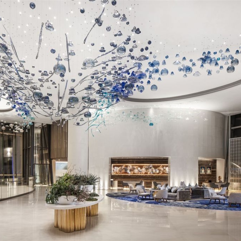 This blue-tone liuli bubble art chandelier is composed of gradient blue and transparent glass bubbles intertwined with metal lines, presenting a dynamic shape like marine plankton. Light refracts through the liuli to emit a transparent and soft halo, serving both lighting and installation art purposes, suitable for high-end commercial spaces such as hotel lobbies and art exhibition halls.