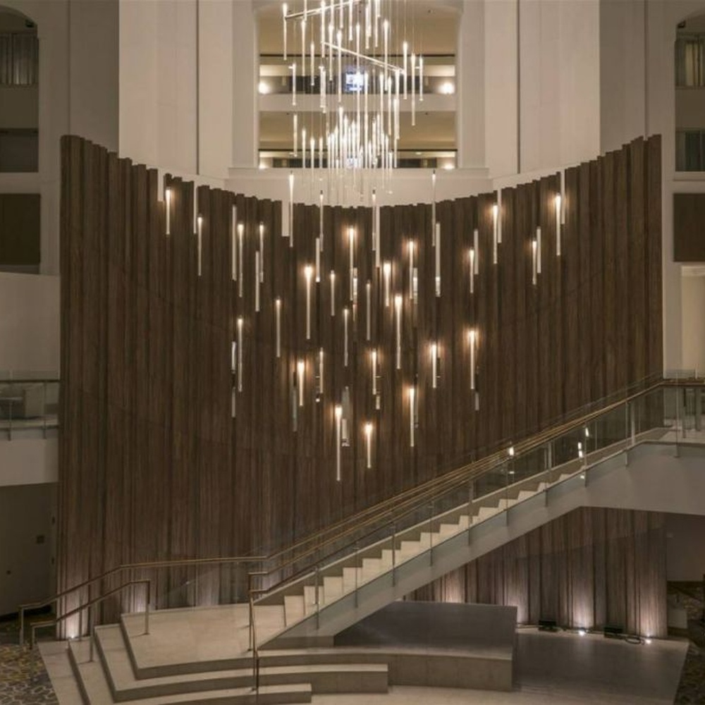 This modern light rain art lighting group consists of a large number of slender linear light strips hanging vertically, creating a "pouring light rain" visual effect with a wooden background wall, serving both lighting and installation art purposes, suitable for high-ceiling commercial spaces such as hotel lobbies and convention centers.