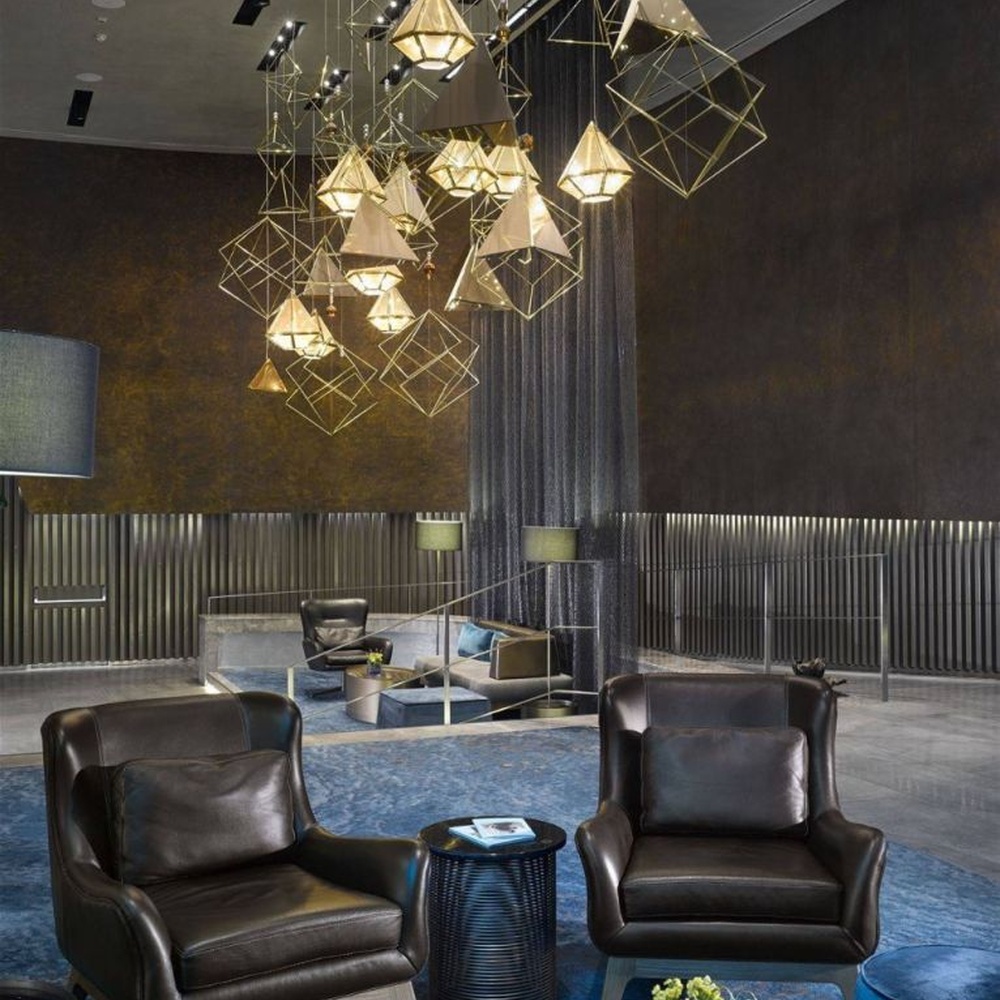 This modern geometric art chandelier is composed of intertwined gold metal lines forming an abstract frame, paired with geometric-shaped liuli/acrylic ornaments. Light refracts through them to emit a brilliant halo, serving both lighting and installation art purposes, suitable for high-ceiling commercial spaces such as hotel lobbies and high-end clubs.