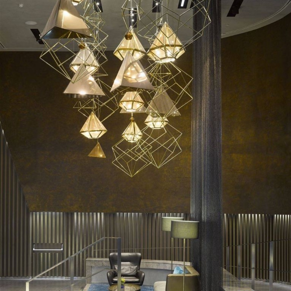 This modern geometric art chandelier is composed of intertwined gold metal lines forming an abstract frame, paired with geometric-shaped liuli/acrylic ornaments. Light refracts through them to emit a brilliant halo, serving both lighting and installation art purposes, suitable for high-ceiling commercial spaces such as hotel lobbies and high-end clubs.