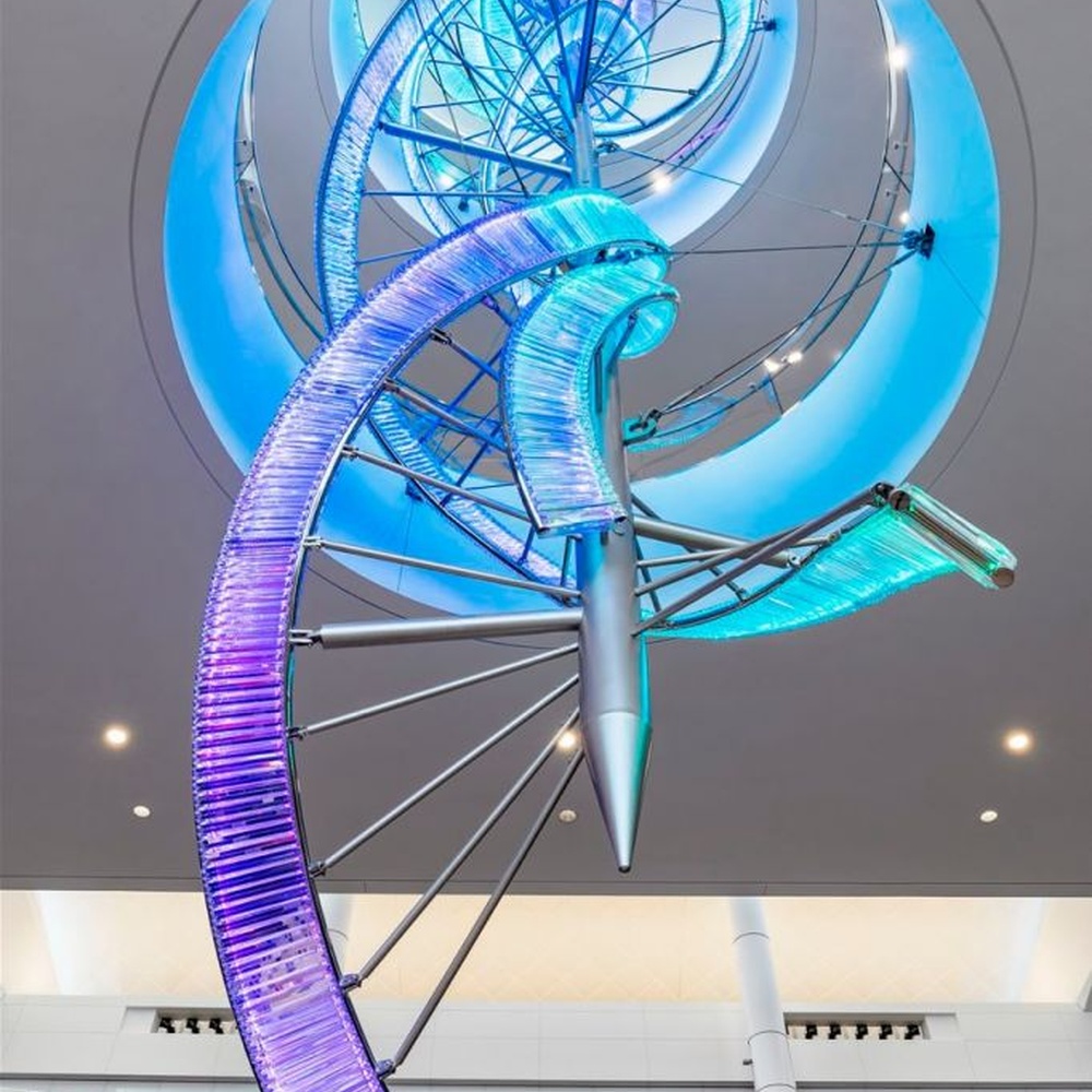 This is a large suspended art installation lamp, supported by a metal frame with blue-purple-cyan gradient LED light strips, featuring an abstract spiral and crescent shape, with both decorative and lighting functions, ideal as artistic decorative lighting for public spaces.