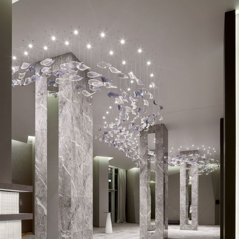 This modern artistic bird-shaped chandelier consists of transparent and gradient blue-purple leaf-shaped glass ornaments hung staggered, arranged in an arc streamline, with point light sources to create a dynamic visual effect, serving both lighting and decorative purposes, suitable for high-end commercial spaces such as luxury sales offices and hotel lobbies.
