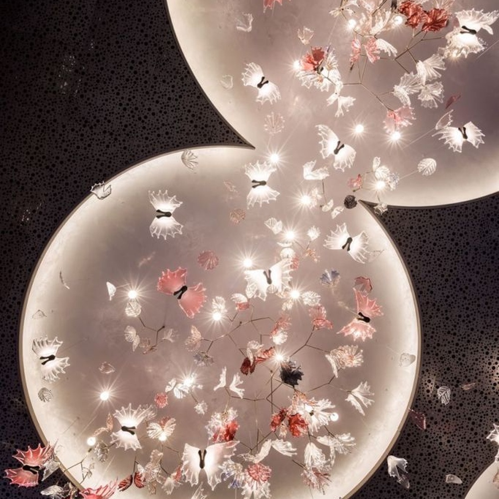 This is a customized artistic flower ceiling chandelier, composed of flower and branch-shaped components made of transparent and red-pink glass/acrylic material, paired with a circular luminous ceiling plate, which has both lighting and artistic decoration functions, suitable for large commercial spaces such as hotel lobbies, banquet halls, and high-end clubs.