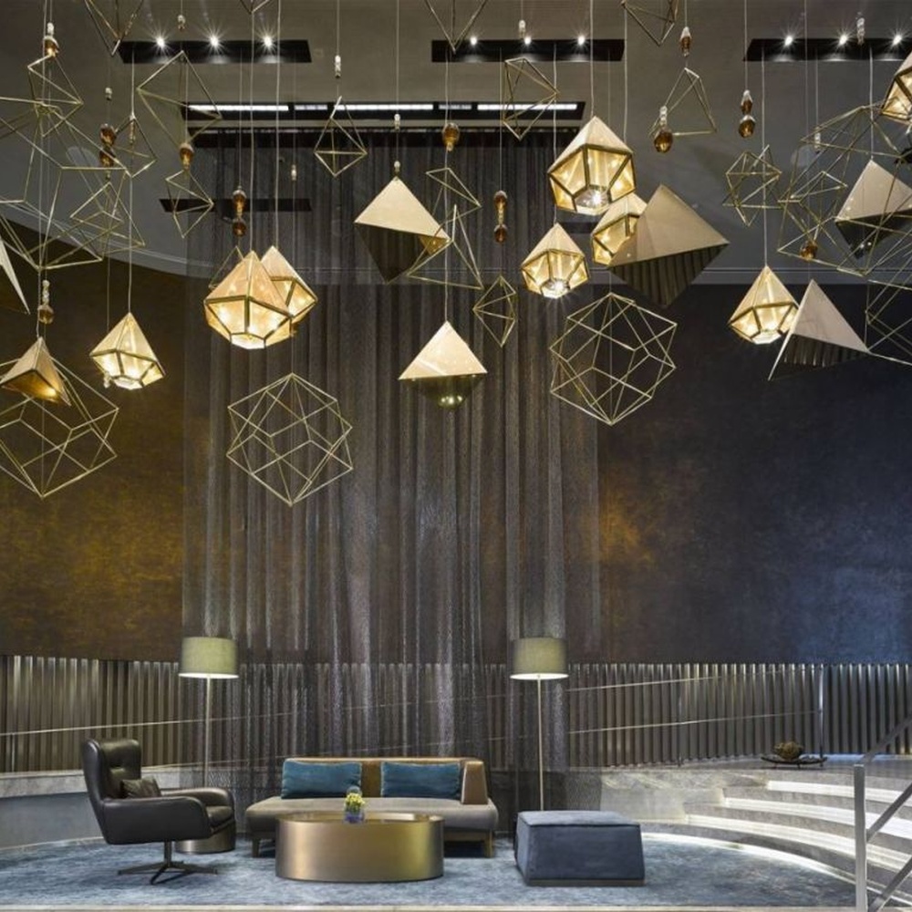 This modern geometric art chandelier is composed of intertwined gold metal lines forming an abstract frame, paired with geometric-shaped liuli/acrylic ornaments. Light refracts through them to emit a brilliant halo, serving both lighting and installation art purposes, suitable for high-ceiling commercial spaces such as hotel lobbies and high-end clubs.