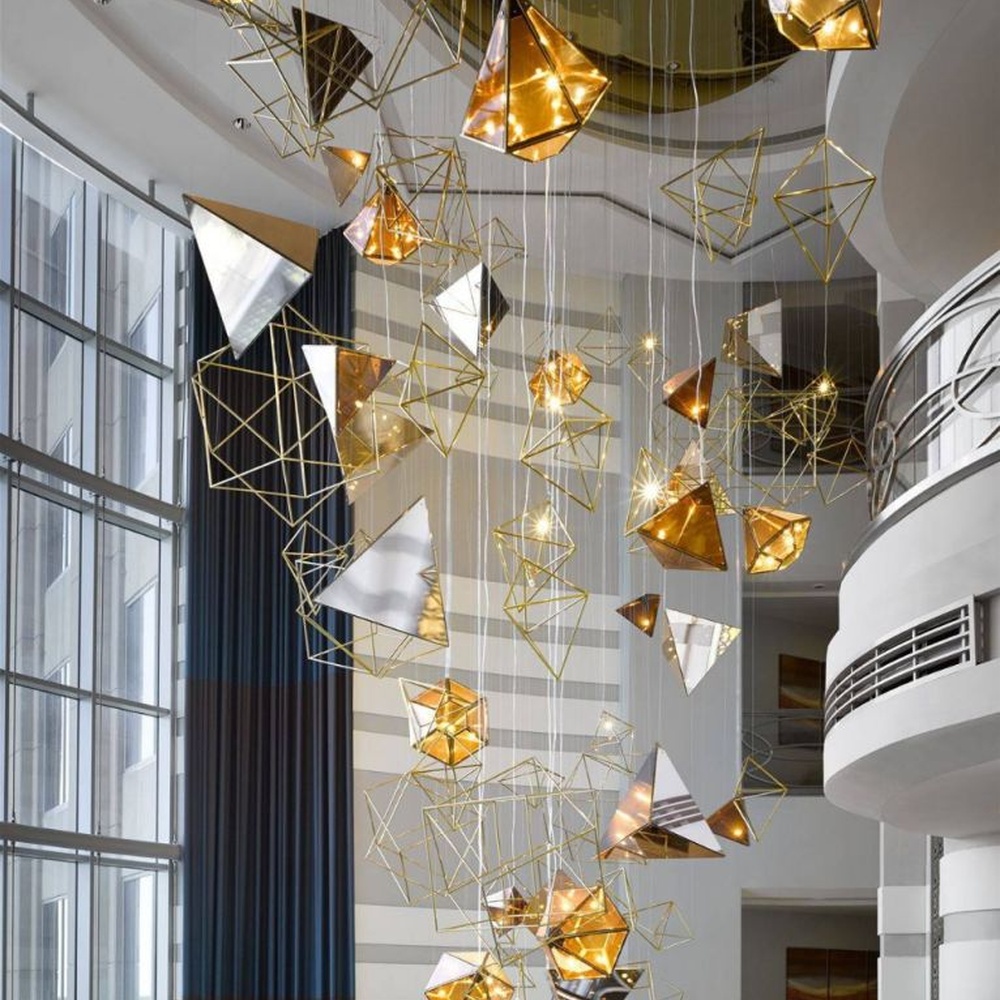 This modern geometric art chandelier is composed of intertwined gold metal lines forming an abstract frame, paired with geometric-shaped liuli/acrylic ornaments. Light refracts through them to emit a brilliant halo, serving both lighting and installation art purposes, suitable for high-ceiling commercial spaces such as hotel lobbies and high-end clubs.