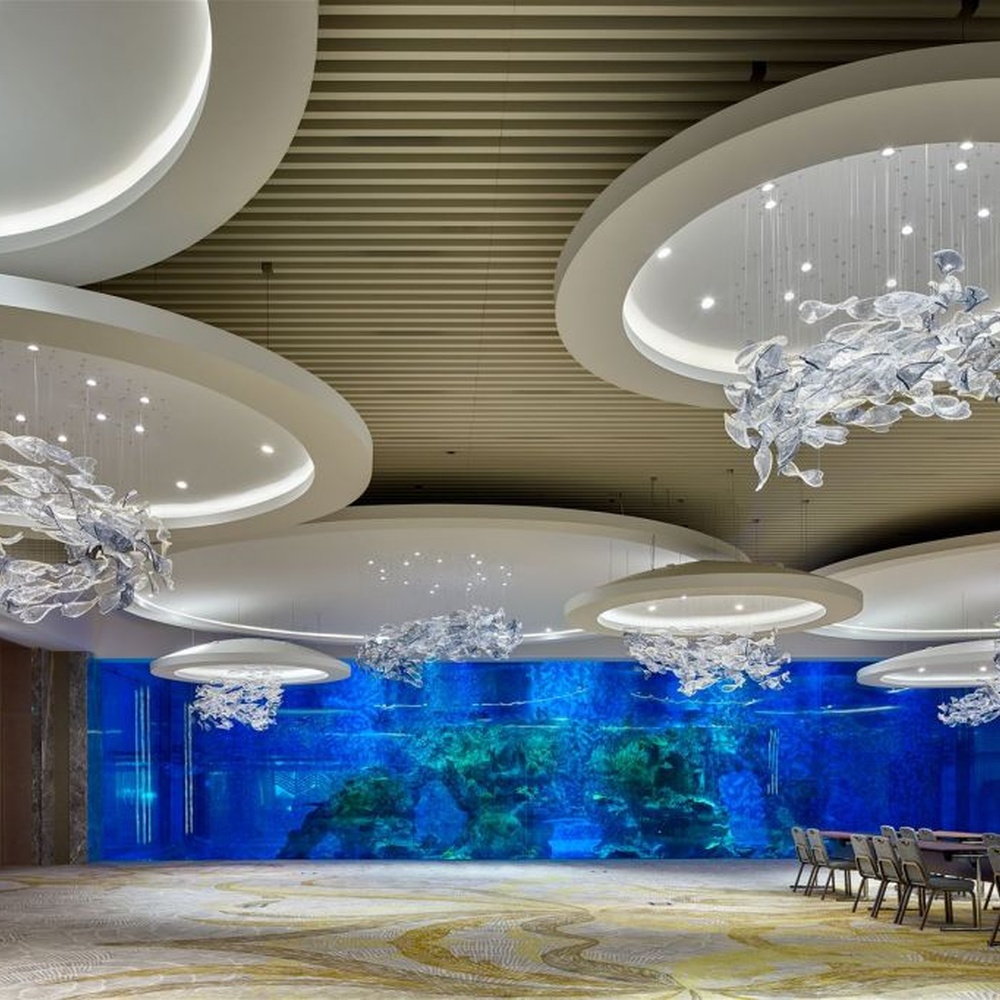 This modern artistic bird-shaped chandelier consists of transparent and gradient blue-purple leaf-shaped glass ornaments hung staggered, arranged in an arc streamline, with point light sources to create a dynamic visual effect, serving both lighting and decorative purposes, suitable for high-end commercial spaces such as luxury sales offices and hotel lobbies.
