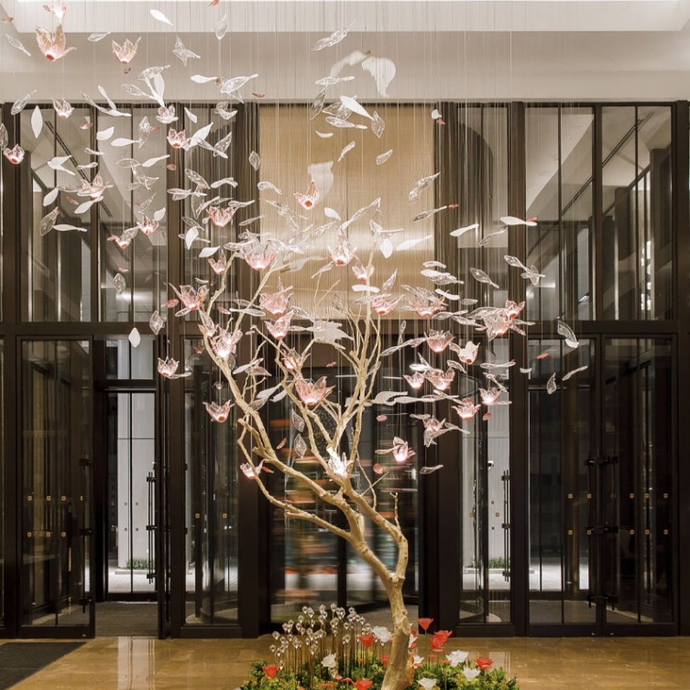 This is an art-installation style tree-shaped chandelier, with a simulated branch as the main structure, paired with transparent and pink-white gradient leaf-shaped luminous components, which has both artistic decoration and soft lighting functions, suitable for large commercial spaces such as hotel lobbies, high-end clubs, and art exhibition halls.