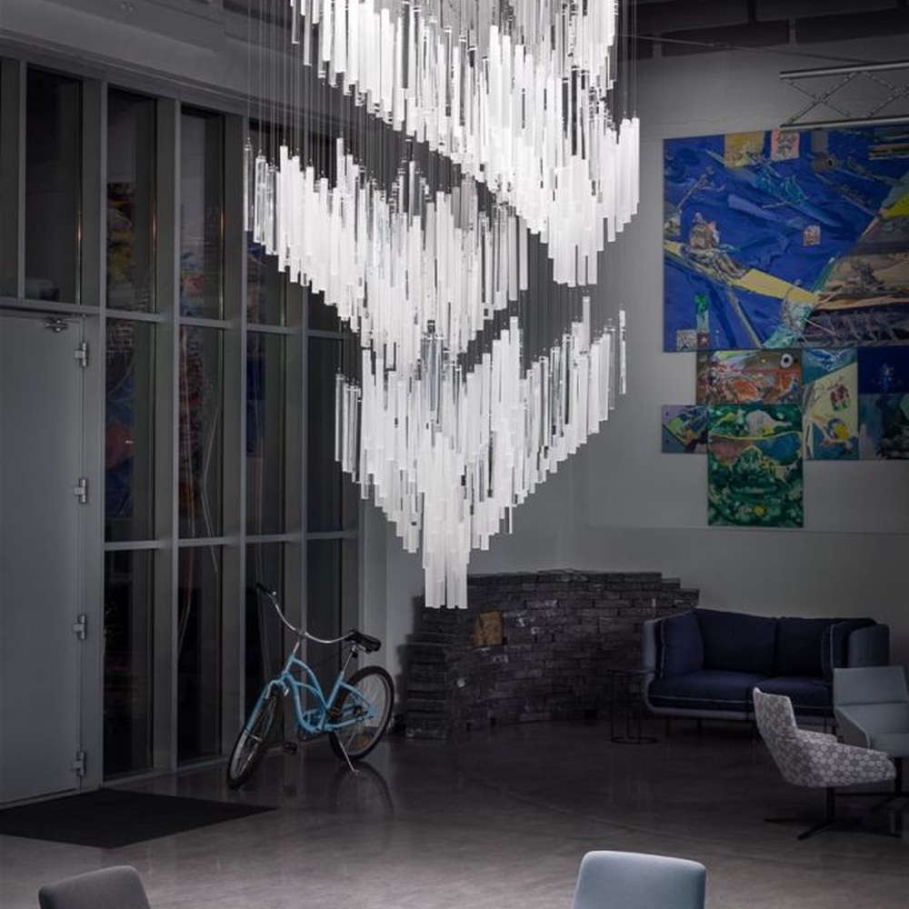 This modern industrial-style art chandelier consists of a large number of white acrylic strips hung staggered by metal wires, extending downward in a waterfall shape from a circular ceiling plate. Light passes through the strips to emit a transparent and soft halo, serving both lighting and decorative purposes, suitable for high-ceiling commercial spaces such as cultural and creative parks and art exhibition halls.