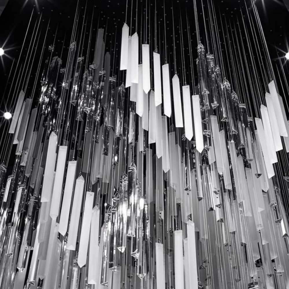 This modern industrial-style art chandelier consists of a large number of white acrylic strips hung staggered by metal wires, extending downward in a waterfall shape from a circular ceiling plate. Light passes through the strips to emit a transparent and soft halo, serving both lighting and decorative purposes, suitable for high-ceiling commercial spaces such as cultural and creative parks and art exhibition halls.
