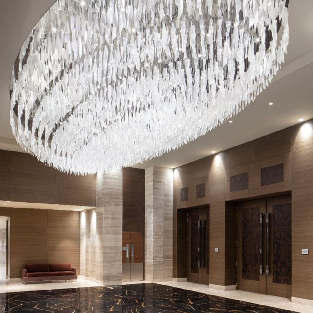This large oval artistic chandelier is composed of a large number of transparent glass/acrylic pieces hung in a staggered manner, presenting a fluffy and soft visual effect like a cloud. The light refracts through the material to emit a brilliant and transparent glow, serving both lighting and decorative purposes, suitable for core decoration and lighting in large spaces such as hotel lobbies and high-end clubs.