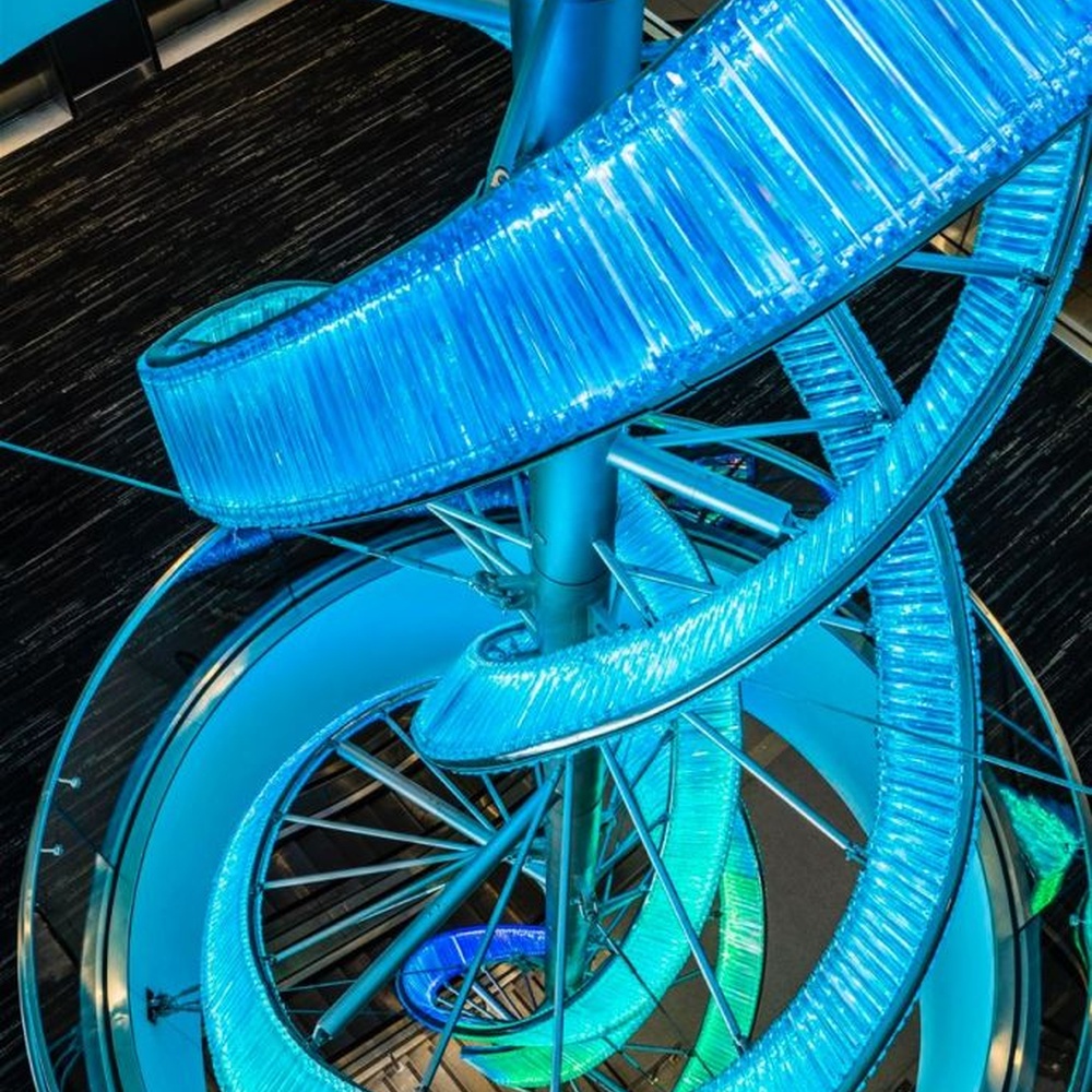 This is a large suspended art installation lamp, supported by a metal frame with blue-purple-cyan gradient LED light strips, featuring an abstract spiral and crescent shape, with both decorative and lighting functions, ideal as artistic decorative lighting for public spaces.