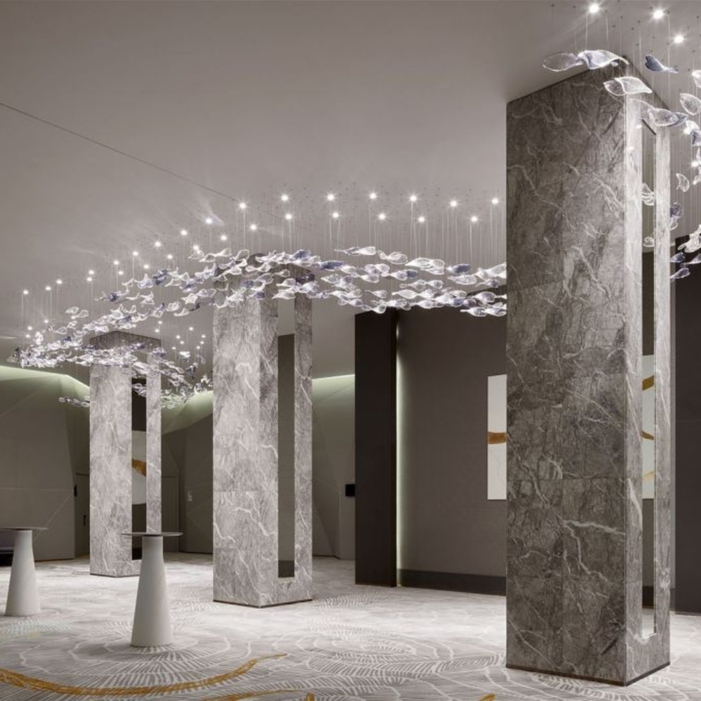 This modern artistic bird-shaped chandelier consists of transparent and gradient blue-purple leaf-shaped glass ornaments hung staggered, arranged in an arc streamline, with point light sources to create a dynamic visual effect, serving both lighting and decorative purposes, suitable for high-end commercial spaces such as luxury sales offices and hotel lobbies.
