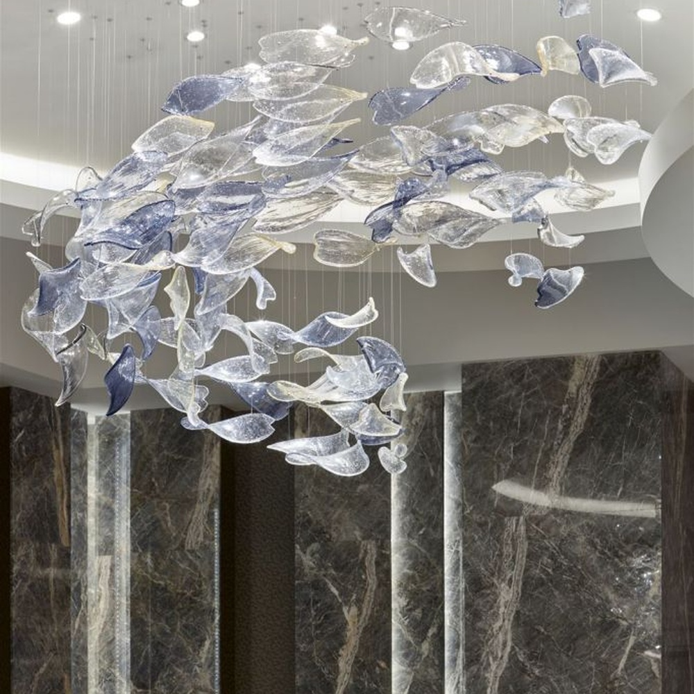 This modern artistic bird-shaped chandelier consists of transparent and gradient blue-purple leaf-shaped glass ornaments hung staggered, arranged in an arc streamline, with point light sources to create a dynamic visual effect, serving both lighting and decorative purposes, suitable for high-end commercial spaces such as luxury sales offices and hotel lobbies.
