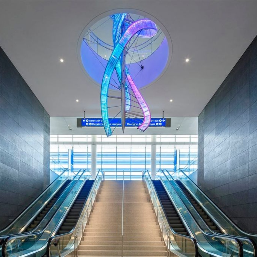 This is a large suspended art installation lamp, supported by a metal frame with blue-purple-cyan gradient LED light strips, featuring an abstract spiral and crescent shape, with both decorative and lighting functions, ideal as artistic decorative lighting for public spaces.