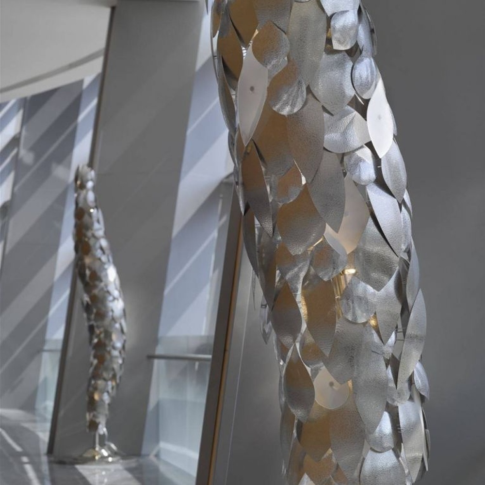 This light luxury art sculpture floor lamp features a twisted scale shape made of metal, with warm light refracting a luxurious halo through the metal texture, serving both lighting and decorative purposes, suitable for luxury spaces such as high-end hotel lobbies and clubs.