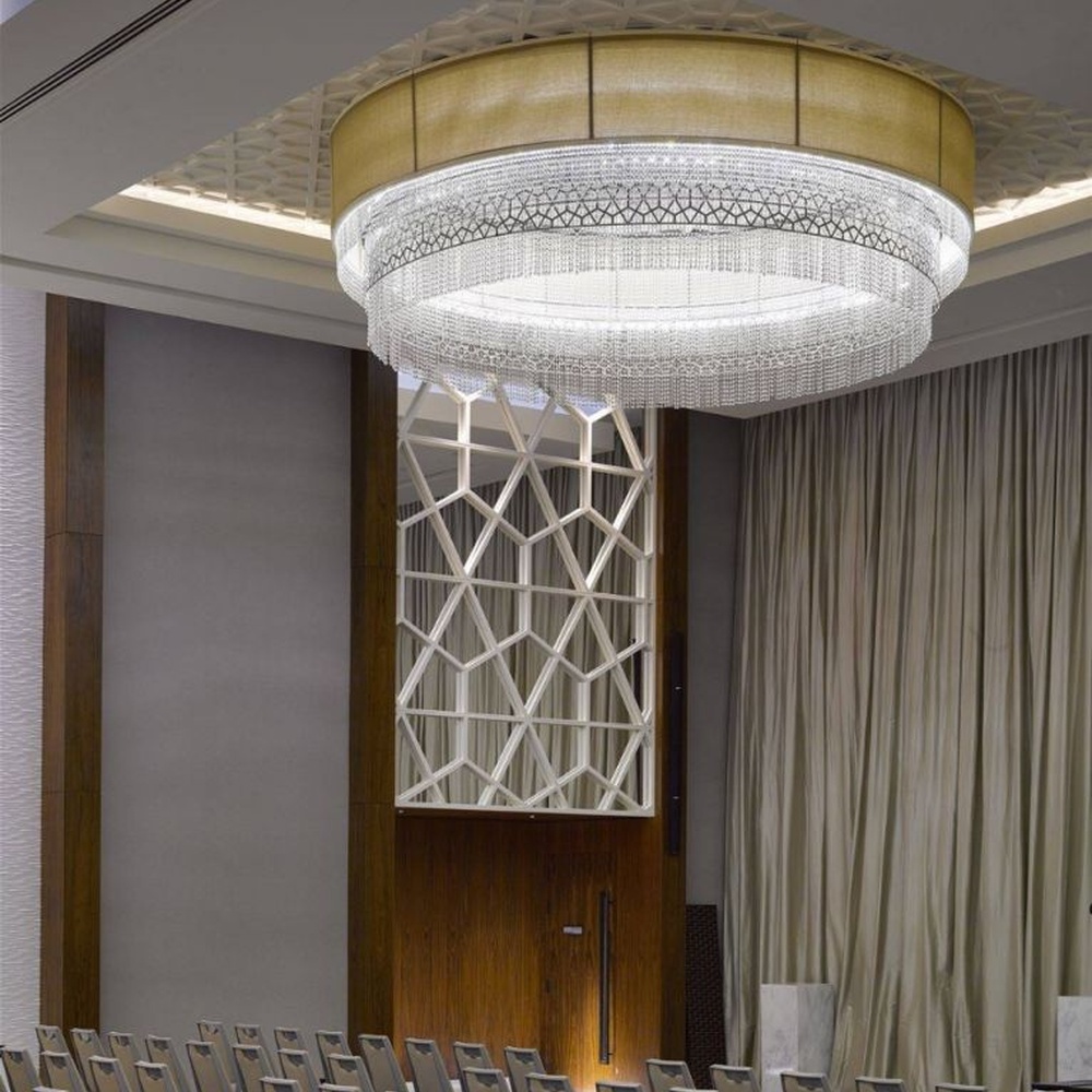 This large multi-layer round crystal ceiling lamp features a gold metal frame paired with multi-layer crystal tassels and a geometric texture lampshade, with light refracting a brilliant halo through the crystals, serving both lighting and decorative purposes, suitable for large high-end commercial spaces such as hotel banquet halls and conference centers.