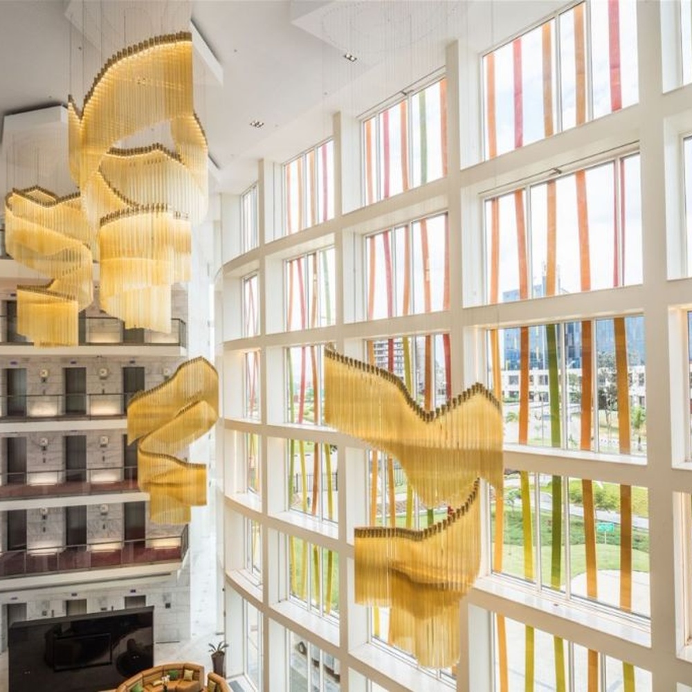 This gilded wave art chandelier is composed of layered gold acrylic strips forming a flowing wave shape, like floating golden ribbons, serving both lighting and installation art purposes, suitable for high-ceiling commercial spaces such as hotel lobbies and convention centers.