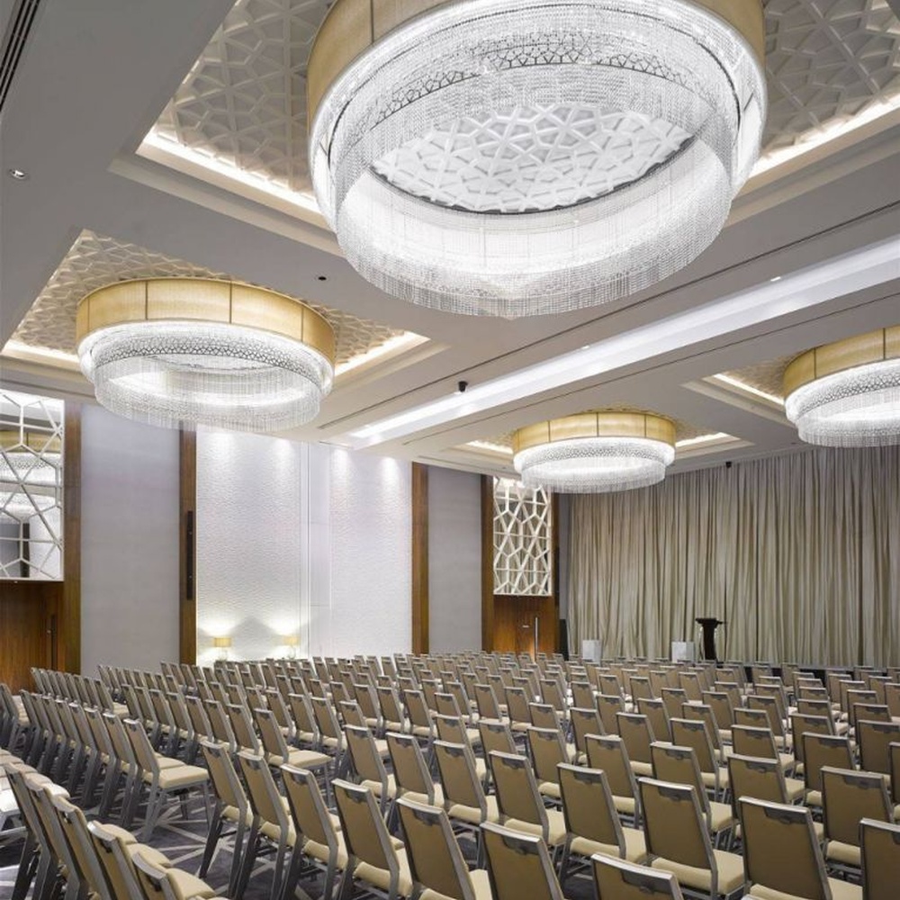 This large multi-layer round crystal ceiling lamp features a gold metal frame paired with multi-layer crystal tassels and a geometric texture lampshade, with light refracting a brilliant halo through the crystals, serving both lighting and decorative purposes, suitable for large high-end commercial spaces such as hotel banquet halls and conference centers.