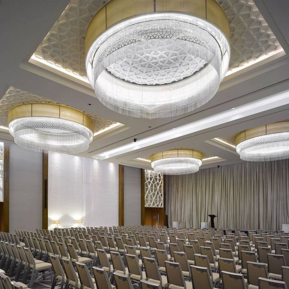 This large multi-layer round crystal ceiling lamp features a gold metal frame paired with multi-layer crystal tassels and a geometric texture lampshade, with light refracting a brilliant halo through the crystals, serving both lighting and decorative purposes, suitable for large high-end commercial spaces such as hotel banquet halls and conference centers.