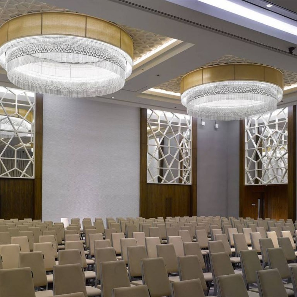 This large multi-layer round crystal ceiling lamp features a gold metal frame paired with multi-layer crystal tassels and a geometric texture lampshade, with light refracting a brilliant halo through the crystals, serving both lighting and decorative purposes, suitable for large high-end commercial spaces such as hotel banquet halls and conference centers.