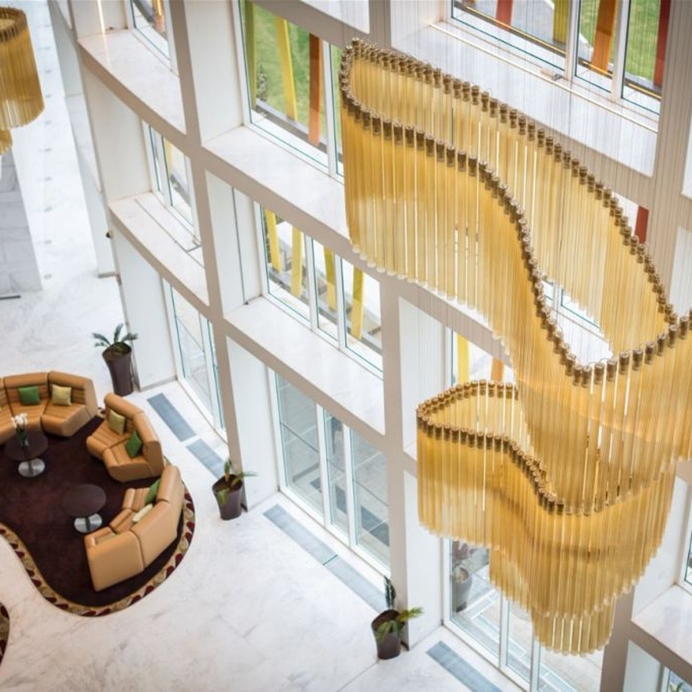 This gilded wave art chandelier is composed of layered gold acrylic strips forming a flowing wave shape, like floating golden ribbons, serving both lighting and installation art purposes, suitable for high-ceiling commercial spaces such as hotel lobbies and convention centers.