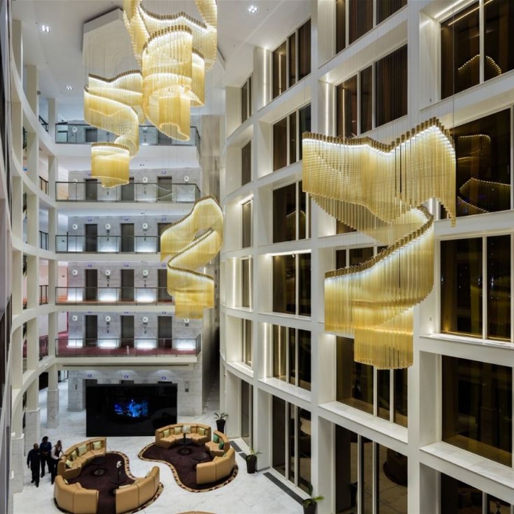 This gilded wave art chandelier is composed of layered gold acrylic strips forming a flowing wave shape, like floating golden ribbons, serving both lighting and installation art purposes, suitable for high-ceiling commercial spaces such as hotel lobbies and convention centers.