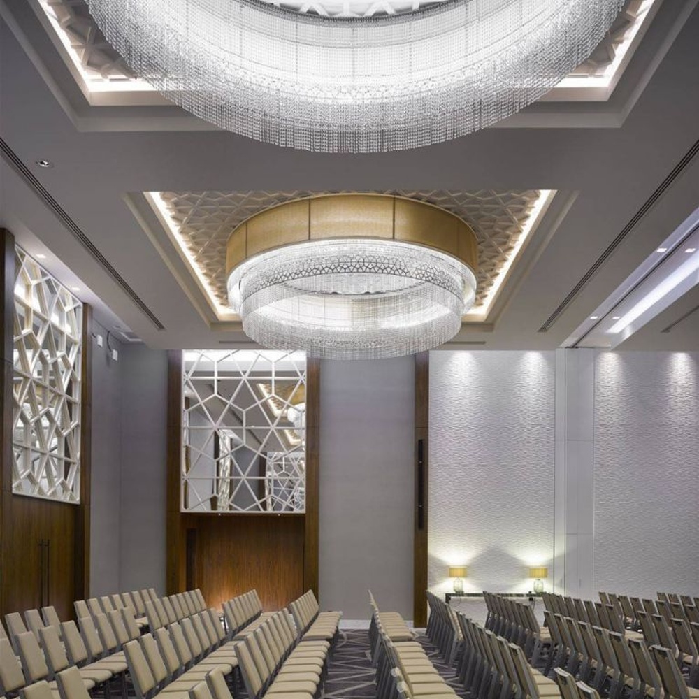 This large multi-layer round crystal ceiling lamp features a gold metal frame paired with multi-layer crystal tassels and a geometric texture lampshade, with light refracting a brilliant halo through the crystals, serving both lighting and decorative purposes, suitable for large high-end commercial spaces such as hotel banquet halls and conference centers.