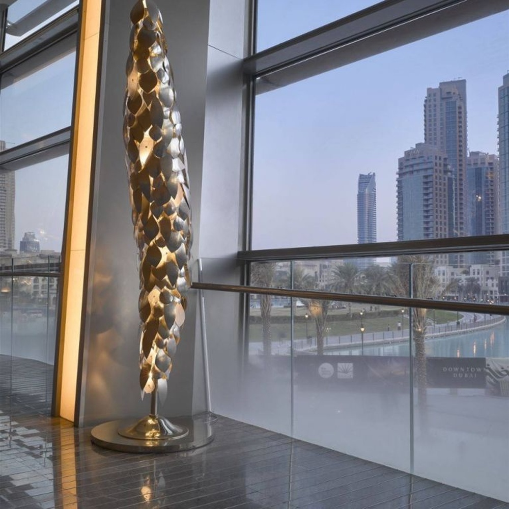 This light luxury art sculpture floor lamp features a twisted scale shape made of metal, with warm light refracting a luxurious halo through the metal texture, serving both lighting and decorative purposes, suitable for luxury spaces such as high-end hotel lobbies and clubs.