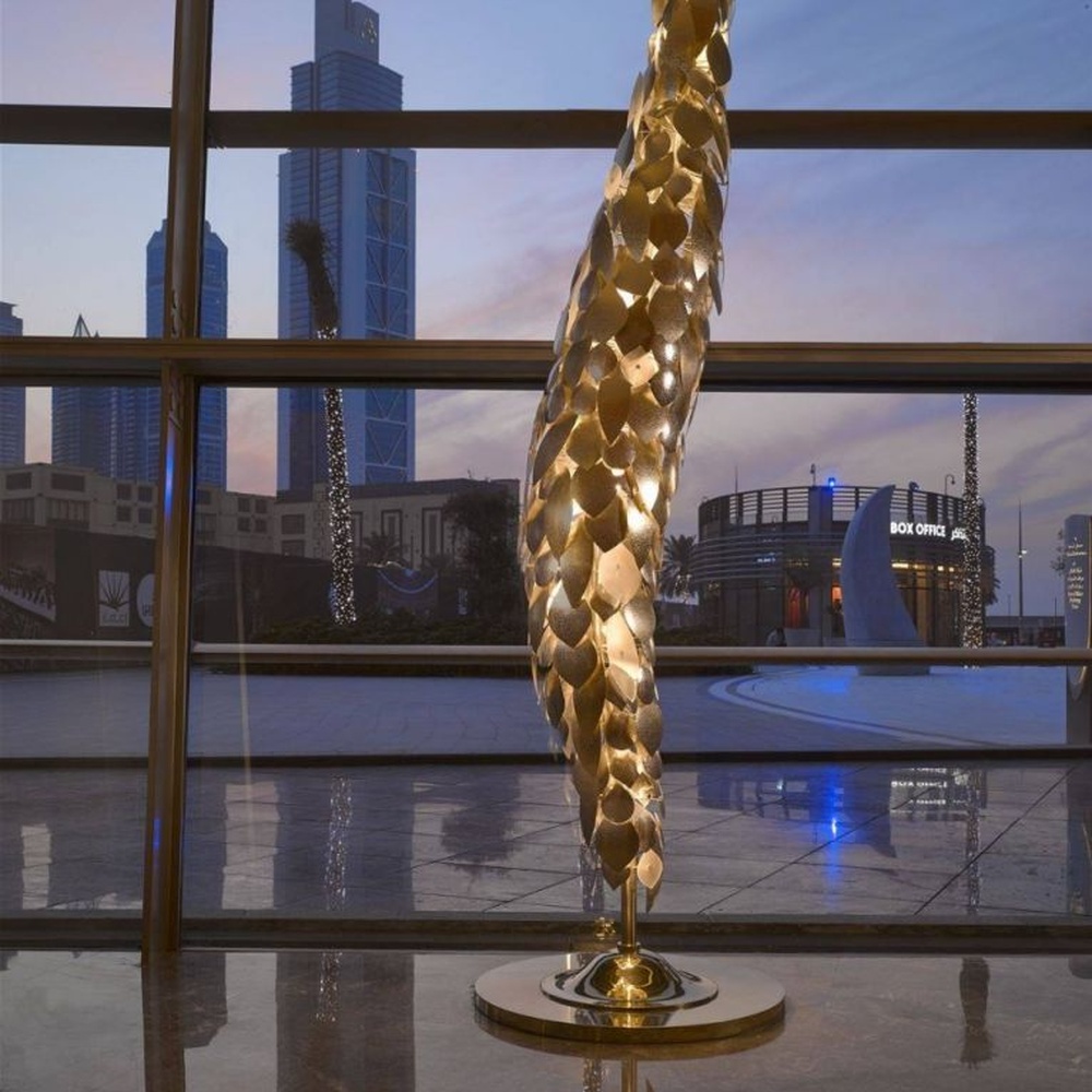 This light luxury art sculpture floor lamp features a twisted scale shape made of metal, with warm light refracting a luxurious halo through the metal texture, serving both lighting and decorative purposes, suitable for luxury spaces such as high-end hotel lobbies and clubs.