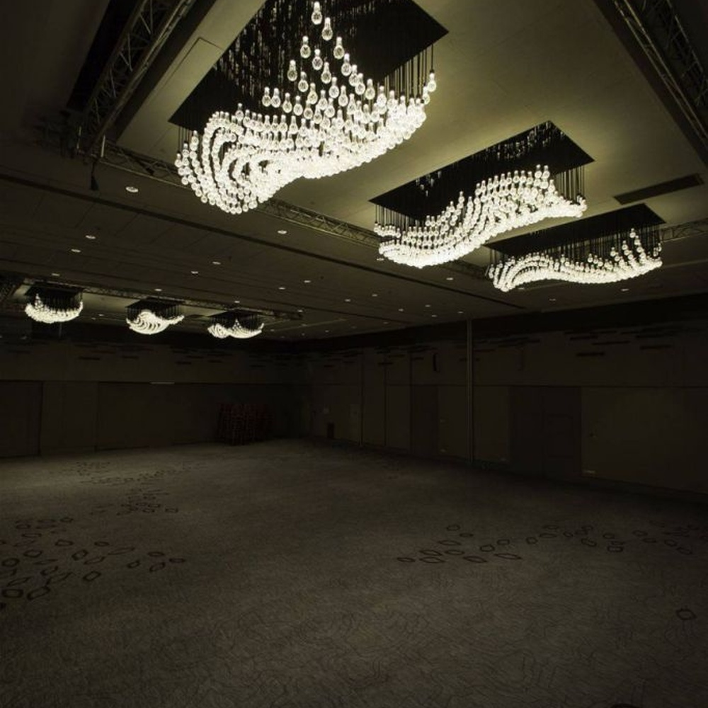 Modern artistic wavy hanging crystal chandelier, with a black metal frame and dense crystal particles creating a flowing wavy shape, combining decorative and main lighting functions, suitable for large-scale commercial spaces such as large banquet halls, exhibition centers, and high-end clubs.