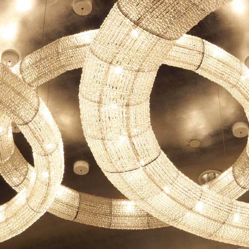 Modern light luxury ring-shaped crystal combination lamp, composed of multiple groups of ring-shaped crystal lamp bodies of different sizes embedded in the ceiling, paired with purple ambient light strips, combining main lighting and atmosphere creation functions, suitable for high-end commercial spaces such as hotel banquet halls and large conference halls.