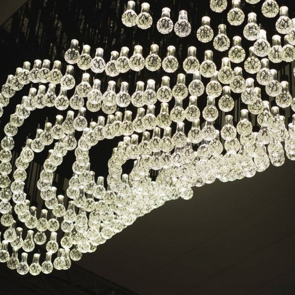 Modern artistic wavy hanging crystal chandelier, with a black metal frame and dense crystal particles creating a flowing wavy shape, combining decorative and main lighting functions, suitable for large-scale commercial spaces such as large banquet halls, exhibition centers, and high-end clubs.