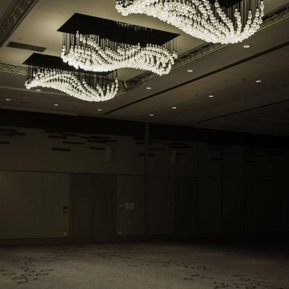 Modern artistic wavy hanging crystal chandelier, with a black metal frame and dense crystal particles creating a flowing wavy shape, combining decorative and main lighting functions, suitable for large-scale commercial spaces such as large banquet halls, exhibition centers, and high-end clubs.