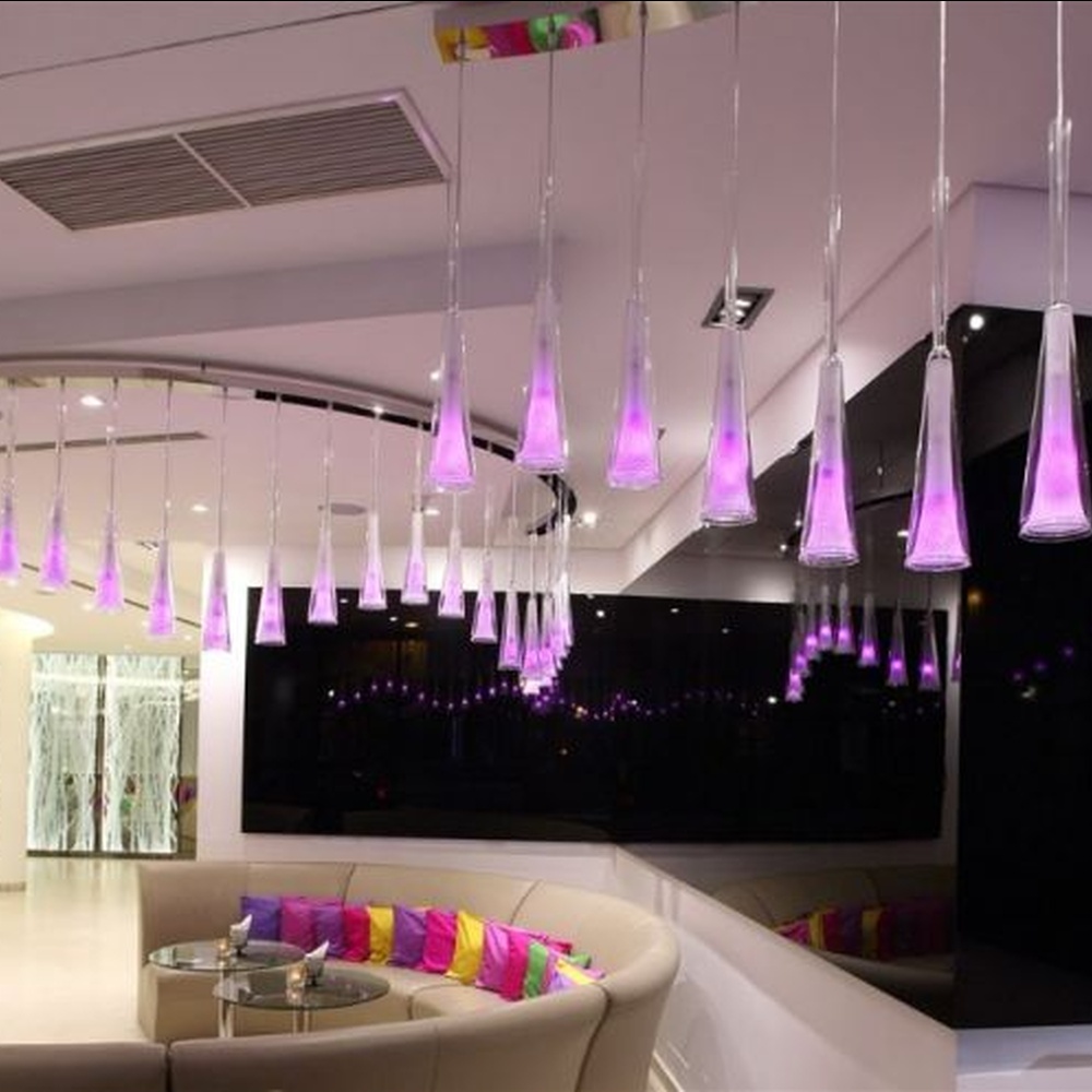 This modern gradient cone LED chandelier features transparent conical lampshades paired with LED gradient pink-purple light sources, arranged in a staggered drooping manner with slender suspension rods, with soft and dreamy light, serving both lighting and decorative purposes, suitable for modern entertainment commercial spaces such as bars and lounges.