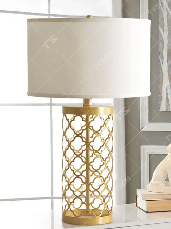 This is a modern minimalist table lamp with a golden base decorated with white vertical strips and a white fabric lampshade, featuring a simple and elegant design. It is used for local desktop lighting and decoration, combining practicality and aesthetics. It is suitable for modern home bedroom bedside tables, living room side tables, high-end hotel guest rooms, luxury apartment living spaces and other places.