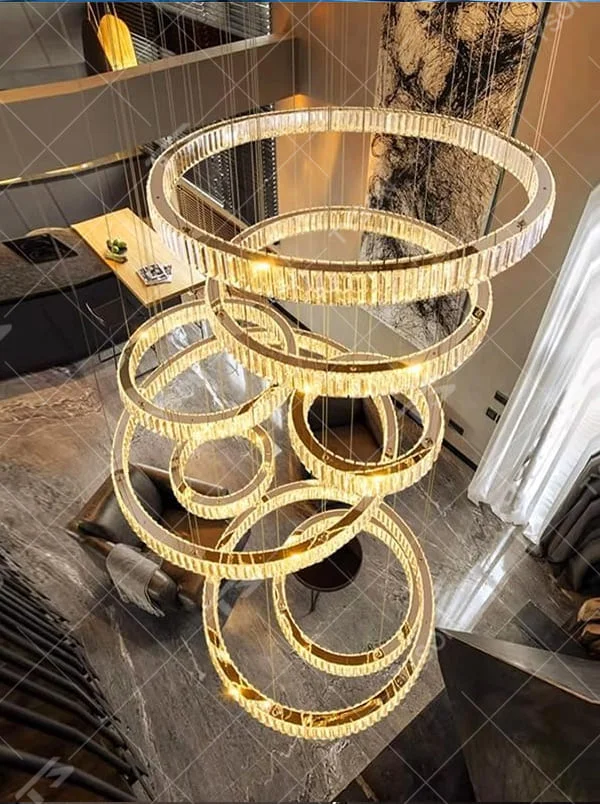 This is a luxury multi-layer circular crystal chandelier, with a golden base and staggered hanging crystal ring lamp bodies. It features a luxurious and grand design, shining brightly under light. It is used for space lighting and decoration, creating a high-end and luxurious ambiance. It is suitable for double-height living rooms in villas, lobbies of high-end hotels, luxury clubs and other places.