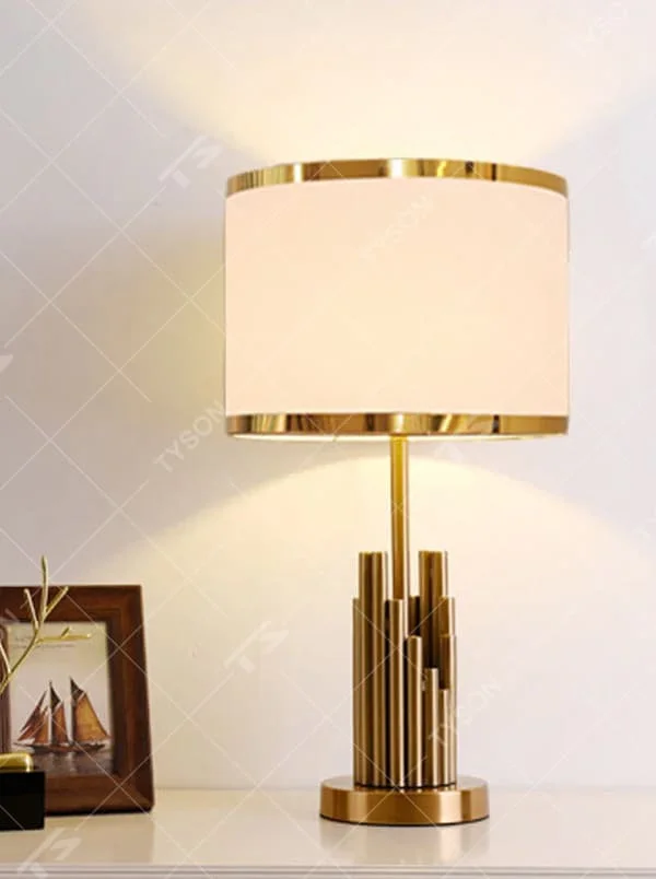 This is a modern luxury-style table lamp with a golden metal multi-column base and a beige fabric lampshade, featuring a simple and elegant design. It is used for local desktop lighting and decoration, combining practicality and aesthetics. It is suitable for modern home bedroom bedside tables, living room side tables, high-end hotel guest rooms, luxury apartment living spaces and other places.