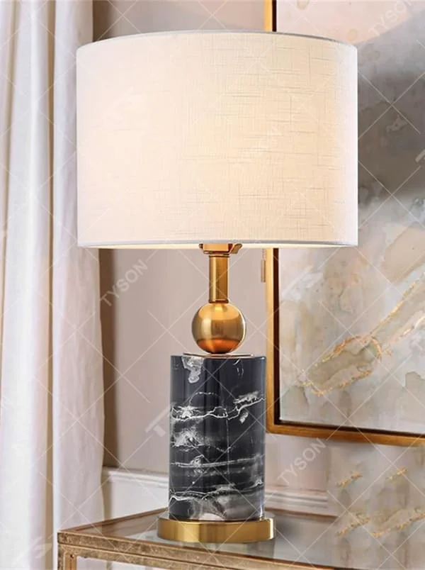 This is a modern minimalist table lamp with a black-and-white marble cylindrical base, a golden spherical decoration and lamp pole, and a white fabric lampshade. It features a simple and elegant design, combining texture and luxury. It is used for local desktop lighting and decoration to enhance the space style. It is suitable for modern home bedroom bedside tables, living room side tables, high-end hotel guest rooms, luxury apartment living spaces and other places.