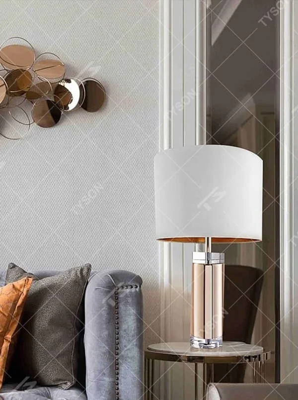 This is a luxury metal crystal table lamp, with a golden metal column, a transparent crystal base, and a white cylindrical fabric lampshade (with golden decoration on top), featuring a luxurious and elegant design with strong modern sense. It is used for local desktop lighting and decoration, creating a high-end luxury atmosphere. It is suitable for luxury-style home bedroom bedside tables, high-end hotel guest rooms, modern soft decoration display spaces and other places.