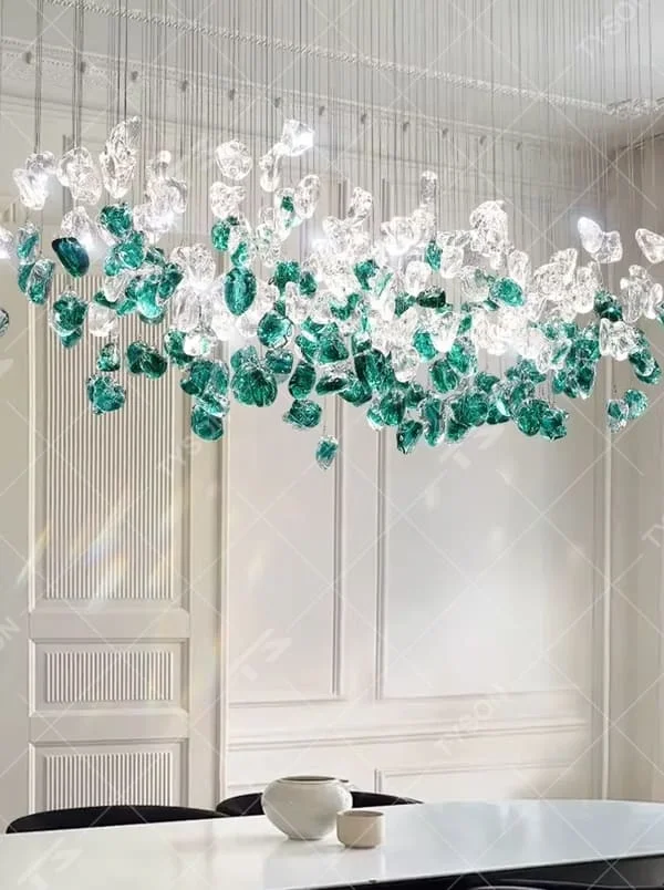 This is an artistic glass stone chandelier, with blue-green and transparent glass stones distributed irregularly in a hanging structure, featuring a modern artistic design with strong luxury artistic sense. It is used for space lighting and decoration, creating an artistic luxury atmosphere. It is suitable for modern luxury home living rooms, art exhibition halls, high-end restaurants and other places.